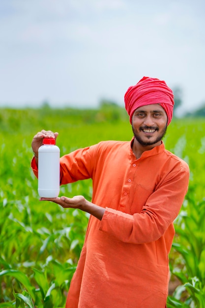 Joven agricultor indio que muestra la botella de fertilizante líquido en el campo de la agricultura.