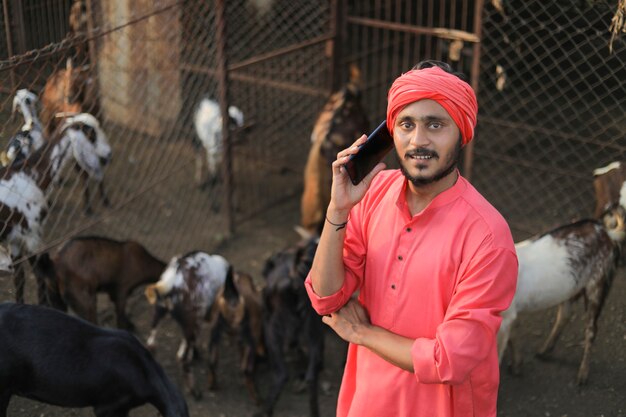 Joven agricultor indio con smartphone en granja lechera de cabras