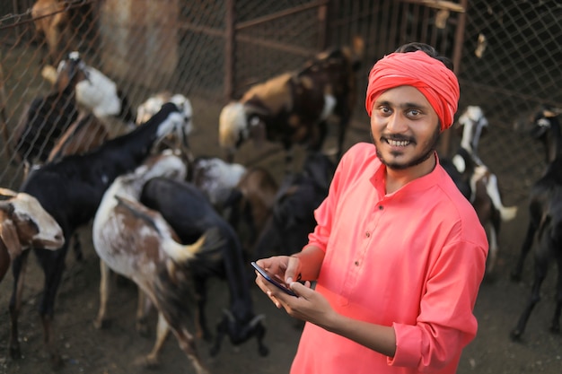 Joven agricultor indio con smartphone en granja lechera de cabras