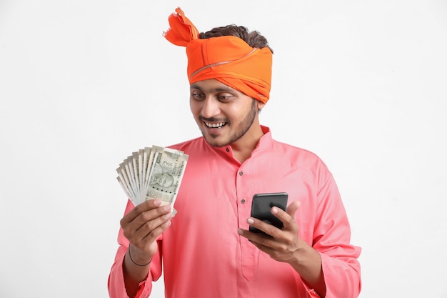 Joven agricultor indio con smartphone y mostrando dinero sobre fondo blanco.