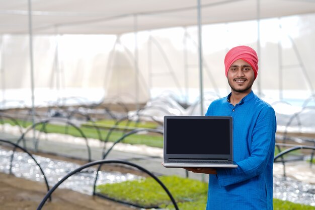 Joven agricultor indio usando laptop en invernadero o casa de polietileno