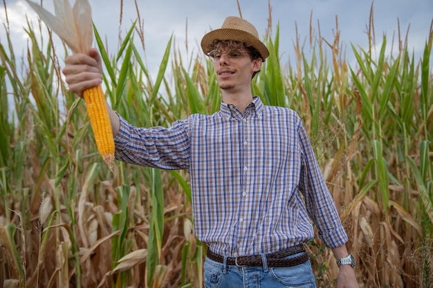 Joven agricultor junto a su campo de maíz muestra con orgullo una gran mazorca de maíz cosechada