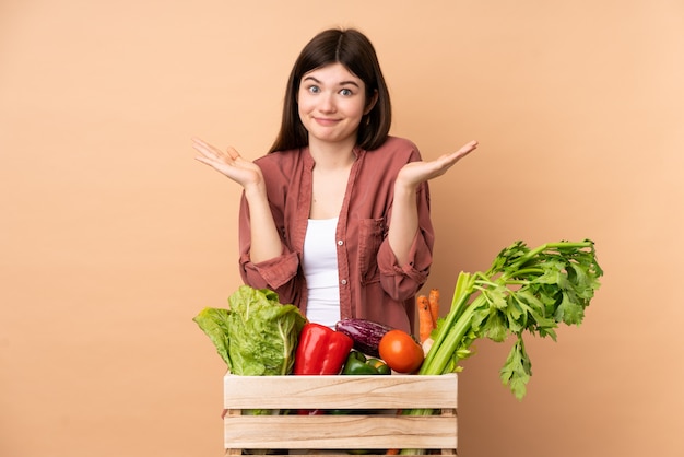 Joven agricultor con verduras recién cosechadas en una caja haciendo dudas gesto