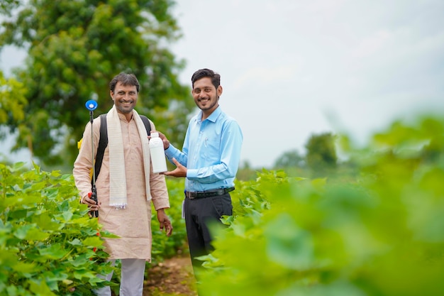 Joven agrónomo indio dando una botella de fertilizante líquido al agricultor y diciendo información del producto en el campo de la agricultura verde.