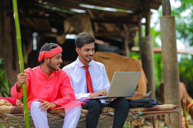 Joven agrónomo indio mostrando alguna información al agricultor en la computadora portátil en casa