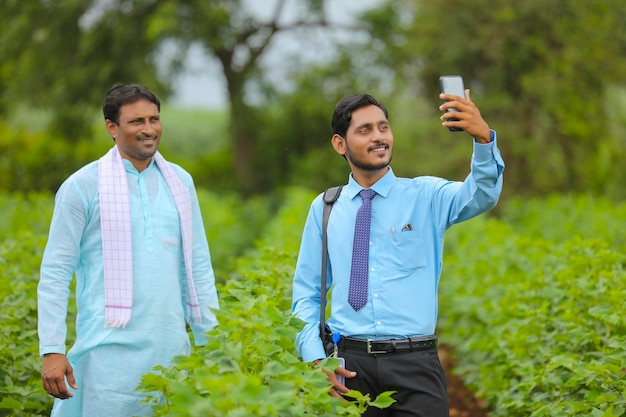 Joven agrónomo o banquero indio tomando selfie con el agricultor en el campo de la agricultura