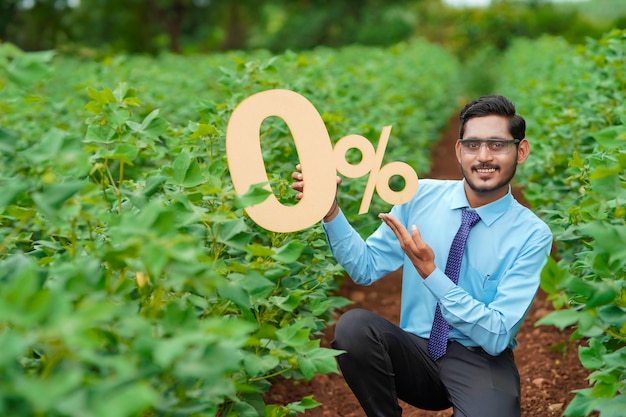 Joven agrónomo o financiero indio que muestra el signo o símbolo del cero por ciento en el campo de la agricultura