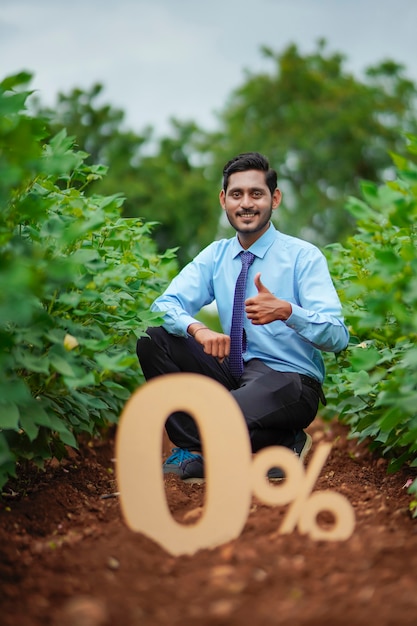 Joven agrónomo o financiero indio que muestra el signo o símbolo del cero por ciento en el campo de la agricultura