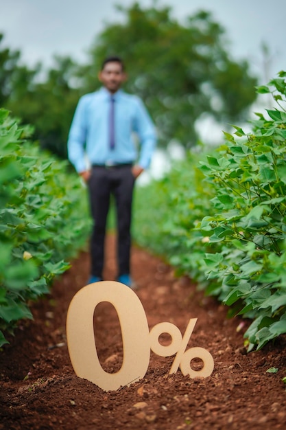 Joven agrónomo o financiero indio que muestra el signo o símbolo del cero por ciento en el campo de la agricultura