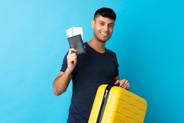 Joven aislado en azul en vacaciones con maleta y pasaporte