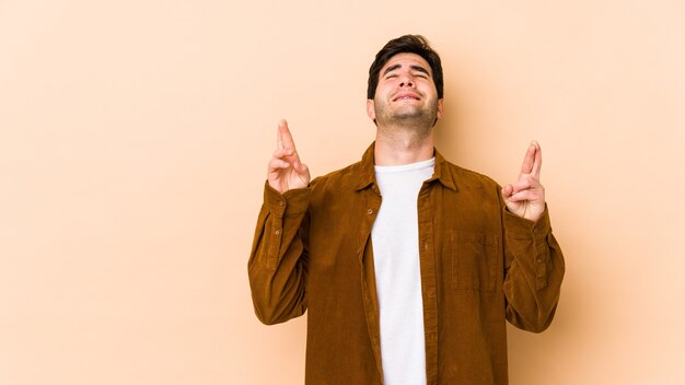 Joven aislado en la pared beige cruzando los dedos para tener suerte