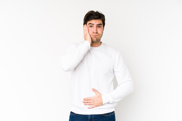 Joven aislado sobre fondo blanco sopla mejillas, tiene expresión cansada. Concepto de expresión facial.