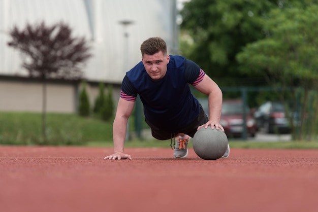 Joven al aire libre realizando flexiones en ejercicio de culturismo con balón medicinal