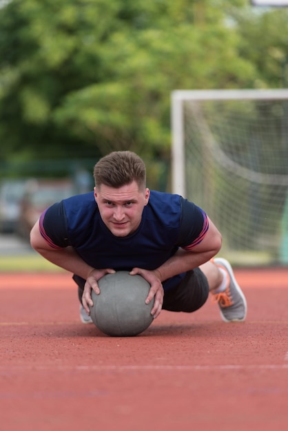 Joven al aire libre realizando flexiones en ejercicio de culturismo con balón medicinal