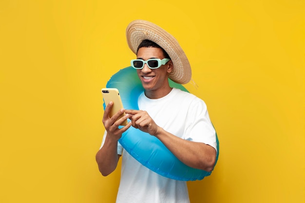 Foto joven alegre afroamericano con anillo de natación inflable utiliza teléfono inteligente en fondo amarillo