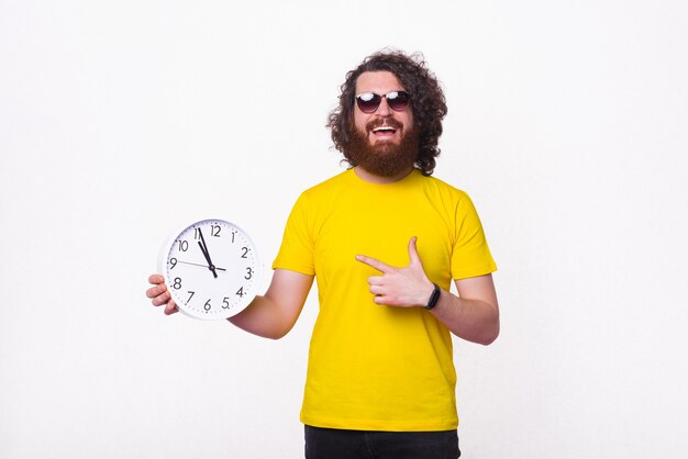 Foto joven alegre está apuntando a un reloj de pared.