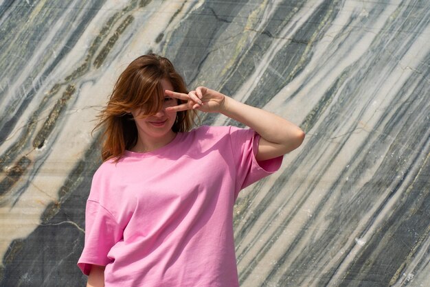 Una joven alegre con una camisa rosa posa con varias expresiones contra un mármol llamativo