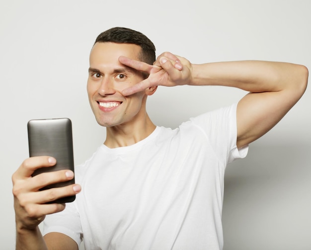 Foto joven alegre con camisa sosteniendo un teléfono móvil y tomando una foto de sí mismo