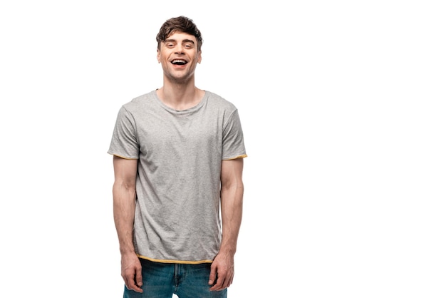 Joven alegre con camiseta gris sonriendo a la cámara aislada en blanco