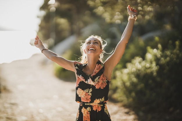 Una joven alegre disfrutando de unas vacaciones de verano y bailando a través de un bosque de pinos cerca del mar.