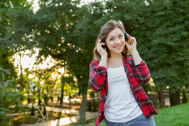 Una joven alegre y divertida escucha música con auriculares en el parque al amanecer.