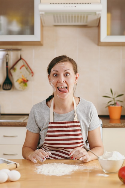 La joven alegre divertida sentada en una mesa con harina y yendo a preparar pasteles en la cocina. Cocinar en casa. Prepara comida.