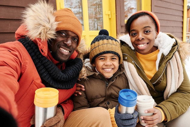 Joven alegre familia afroamericana de tres tomando té caliente junto a su casa