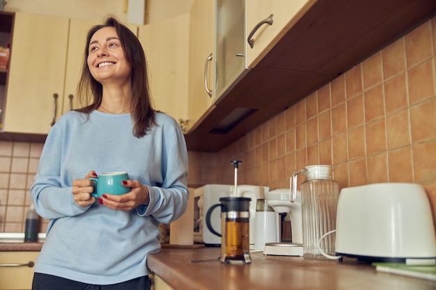 Joven alegre y feliz está preparando un sabroso té en su cocina en casa