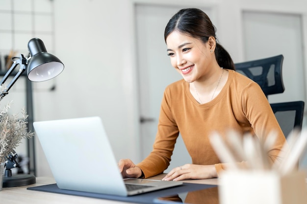 joven alegre feliz positiva linda mujer hermosa sentada en el interior en la oficina de casa usando computadora portátil