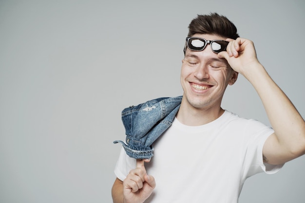 Un joven alegre con gafas de sol en las manos en la cara sonriendo divertidos espectáculos de bromas