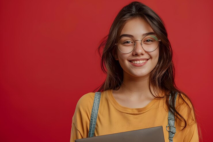 Una joven alegre con gafas sosteniendo un cuaderno contra un fondo rojo vibrante