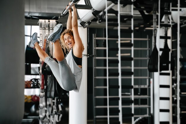 Joven alegre haciendo fitness en las barras de pared del equipo en el gimnasio entrenamiento de espalda y abdominales