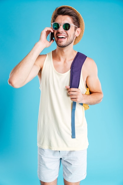 Foto joven alegre con mochila hablando por teléfono celular sobre pared azul