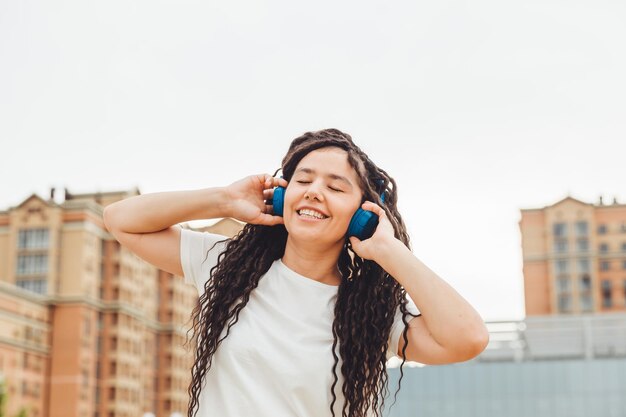 Foto una joven alegre mujer feliz con rastas vestida con una camiseta blanca bailando escuchando música con auriculares descansando relajándose en un parque de la ciudad caminando por un callejón concepto de estilo de vida urbano