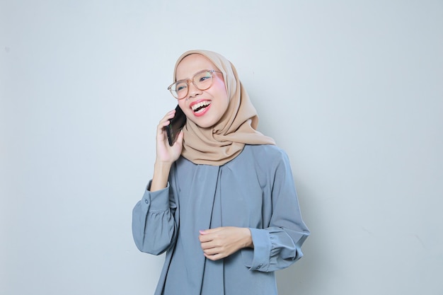 Una joven y alegre mujer de negocios musulmana asiática que usa anteojos usando un teléfono móvil mientras hace una llamada