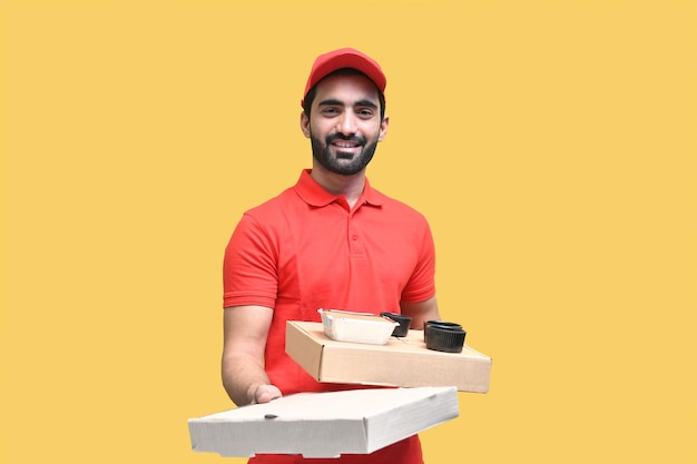 Joven alegre repartidor en camiseta roja sosteniendo cajas de pizza modelo paquistaní indain