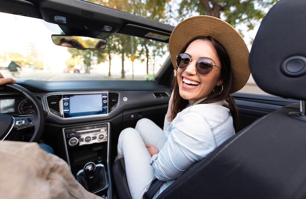 Una joven alegre sentada en un auto convertible sonriendo a la cámara