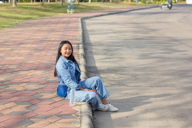 Una joven alegre sentada en el parque de la ciudad sostiene un teléfono móvil con una botella de agua colocada en el concepto de estilo de vida lateral