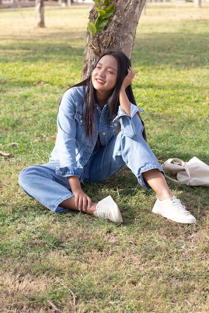 Una joven alegre sentada en el parque sonriendo y usa un concepto de estilo de vida de chaqueta y jeans