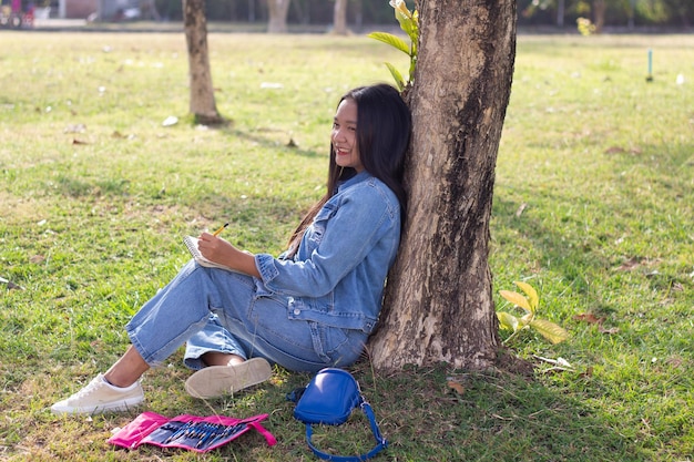 Joven alegre sentado en el parque dibujando ropa de chaqueta y jeans Concepto de vida de la ciudad