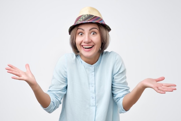 Una joven alegre con sombrero de verano sonriendo a la cámara con las manos abiertas