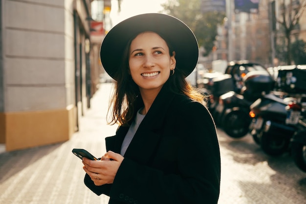 Una joven alegre sostiene su teléfono mientras camina por las calles europeas