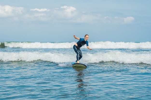 Una joven y alegre surfista principiante con surf azul se divierte en pequeñas olas marinas. Estilo de vida familiar activo, clases de deportes acuáticos al aire libre y actividad de natación en las vacaciones de verano del campamento de surf.