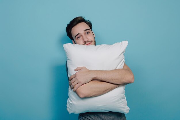 Joven con almohada suave sobre fondo azul durmiendo como un bebé disfrutando de dulces sueños sintiéndose relajado sobre la pared azul