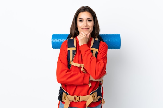 Joven alpinista caucásico con una mochila grande aislada en la pared blanca riendo