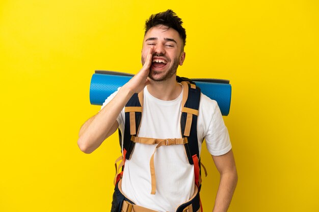 Joven alpinista hombre caucásico con una gran mochila aislada sobre fondo amarillo gritando con la boca abierta