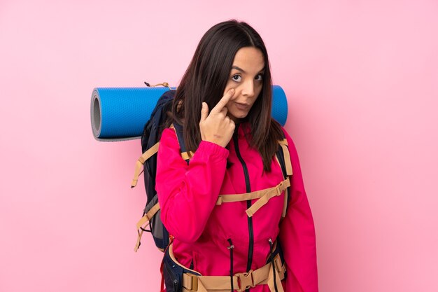 Joven alpinista con una mochila grande sobre fondo rosa aislado mostrando algo