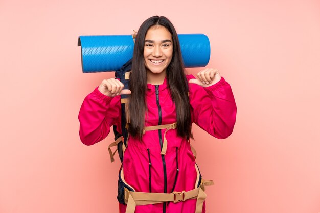 Joven alpinista niña india con una gran mochila aislada sobre fondo rosa orgulloso y satisfecho de sí mismo