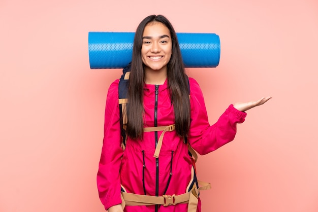Joven alpinista niña india con una gran mochila aislada sobre fondo rosa sosteniendo copyspace imaginario en la palma
