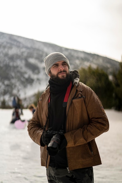 joven alto con barba y cámara fotográfica tomando fotos en la nieve